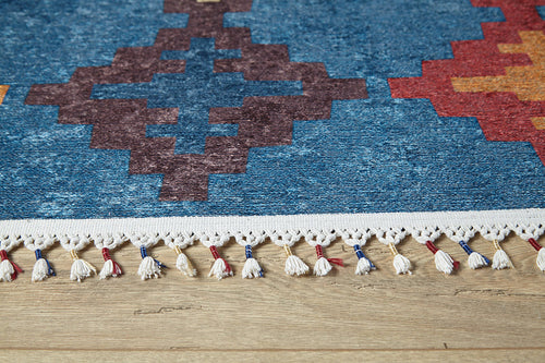 Load image 1 in gallery view. A close-up of the Nomad's Mirage - Washable Rug - JR5032 (Custom Size) shows vibrant blue, red, and orange geometric patterns with white fringe tassels featuring red and blue accents—ideal for high-traffic areas on wooden floors.