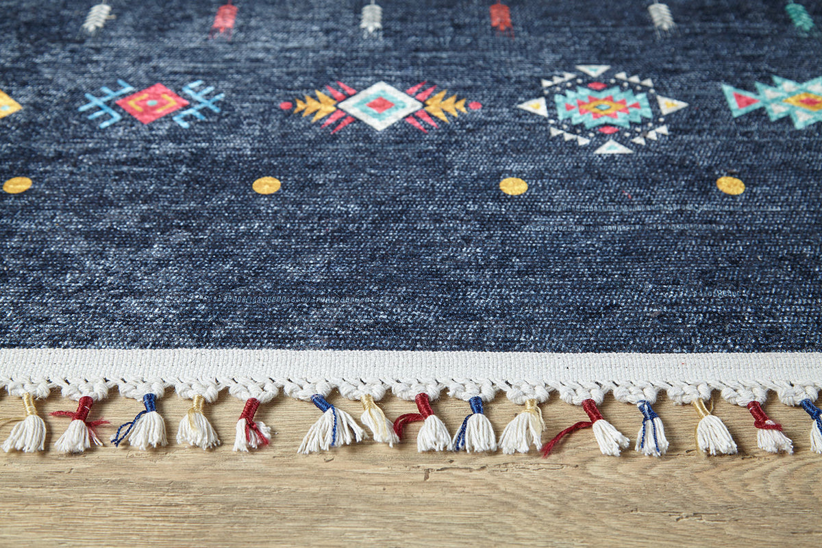 A close-up of the Wanderer's Way - Washable Rug - JR5101 (Custom Size) in dark blue with colorful geometric patterns and white, red, and blue tassels, shown on a wooden floor—perfect for high-traffic areas.