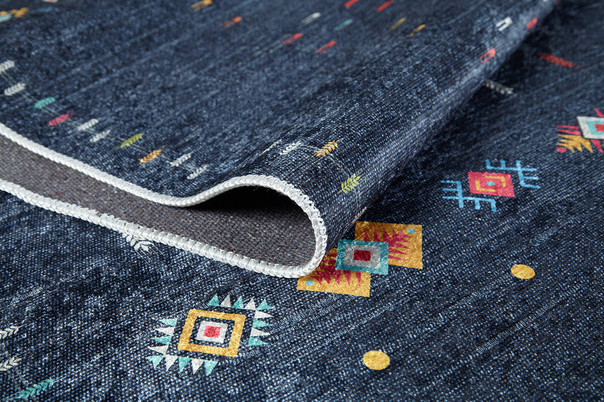 A close-up of the Wanderer's Way - Washable Rug - JR5101 (Custom Size) in dark blue, featuring colorful geometric and tribal patterns, a folded corner showing the back and white stitched edging—ideal for high-traffic areas.