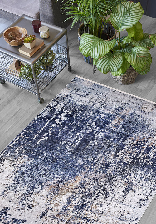 Load image 1 in gallery view. A living room featuring the Abstract Atmosphere - Washable Rug - JR834 in blue and white, a metal coffee table with decor and a plant beneath it, two large leafy green potted plants, all on a light wood floor.