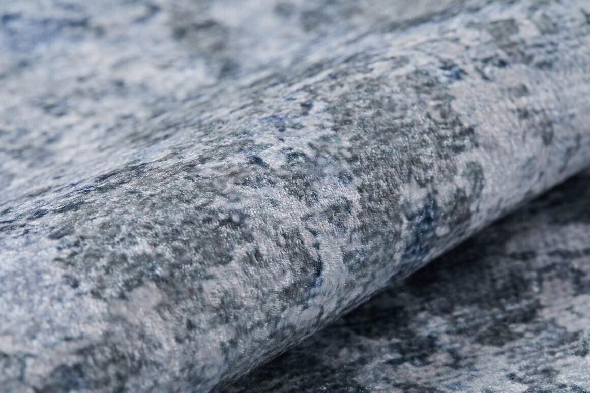 Close-up of Abstract Oasis - Washable Rug - JR144 (Outlet) US, featuring a rolled-up, textured surface in mottled blue, gray, and white—perfect for allergy-sensitive homes or high-traffic areas.