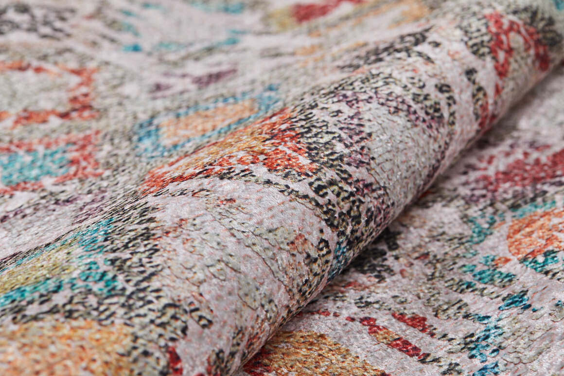 A close-up of the Aged Mosaic - Washable Rug - JR1096 shows its rolled edge and a blend of abstract red, orange, blue, and beige patterns. The flat weave features soft fabric with a slightly raised texture for added depth.