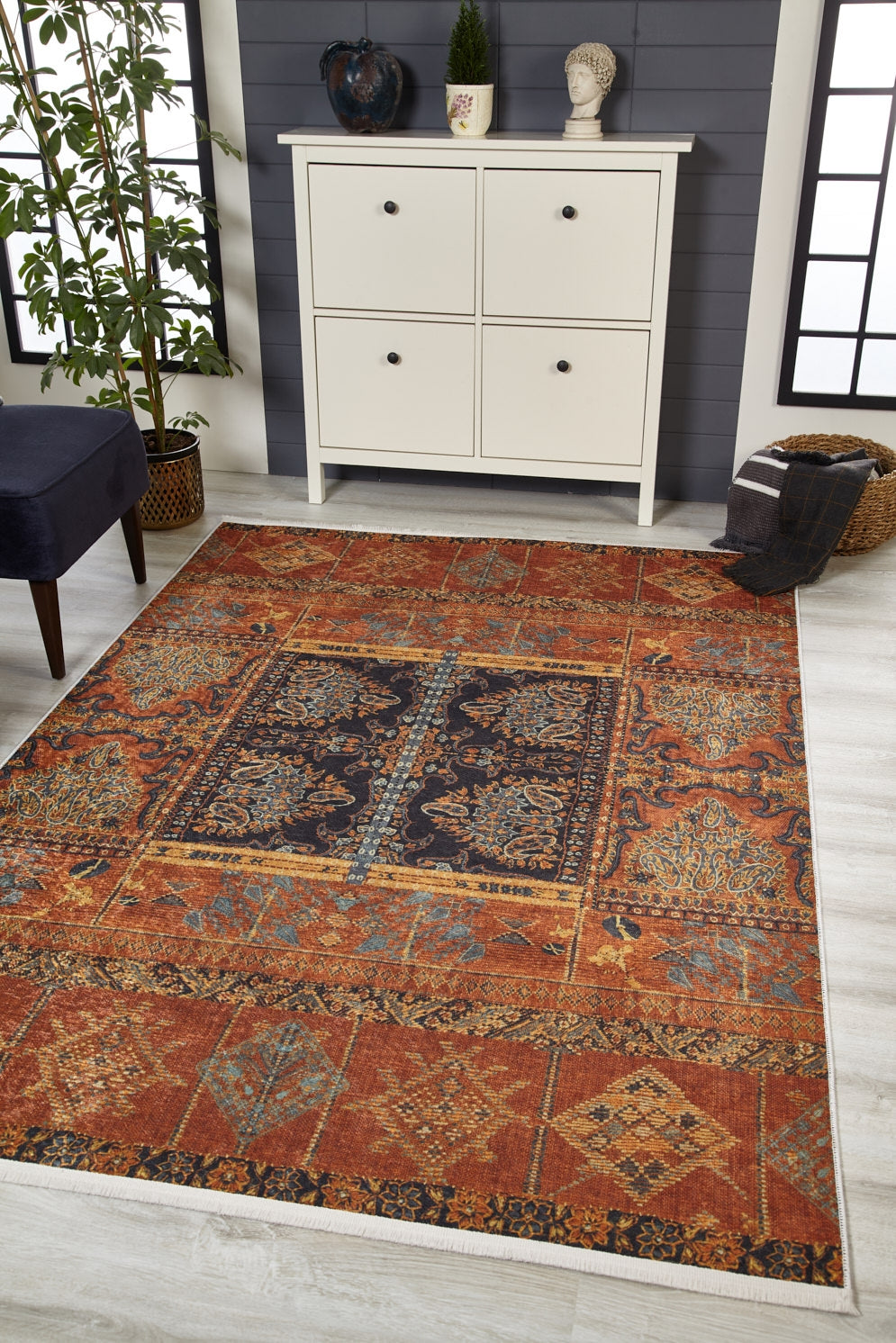 A room with a white four-drawer cabinet, decorative items, a potted plant, a navy chair, and the Ancient Palace - Washable Rug - JR1864—ideal for high-traffic areas—adds warmth to the light wood floor against a dark accent wall.