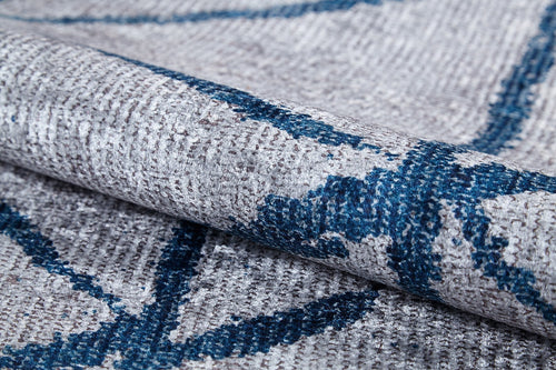 Load image 1 in gallery view. A close-up of the Arabesque Trellis - Washable Rug - JR1732 shows its folded, textured gray fabric with a woven pattern and blue abstract lines. This washable rug has visible stitching, a slightly rough surface, and is ideal for allergy-sensitive homes.