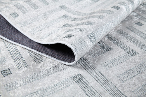 Load image 1 in gallery view. A close-up of the Art Deco Chic - Washable Rug - JR1832 shows its modern gray geometric design, with one corner folded to display the dark textured backing and edge stitching, emphasizing its practical washable construction.
