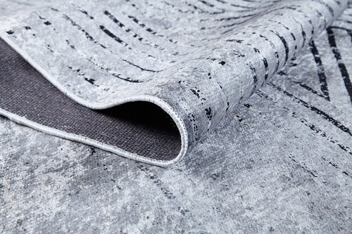 Load image 1 in gallery view. A close-up of the Art Deco Empress - Washable Rug (JR1867) shows its gray-anthracite, textured surface with abstract wavy black lines. A corner is lifted to display the dark backing—ideal for high-traffic, easy-care spaces.