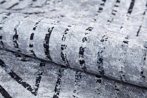 Load image 1 in gallery view. A close-up of the Art Deco Empress - Washable Rug - JR1867 in gray-anthracite, featuring black, irregular vertical lines and a soft, velvety surface. Rolled to show its flexible, plush texture—ideal for high-traffic areas.
