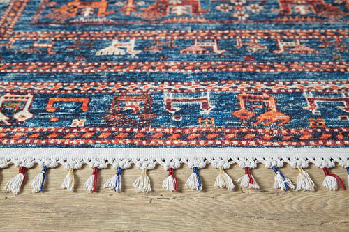 Load image 1 in gallery view. A close-up of the Berber Beauty - Washable Rug - JR5092, featuring blue with red and cream geometric patterns and colorful tassels on the edge, placed on a wooden floor—ideal for high-traffic areas.