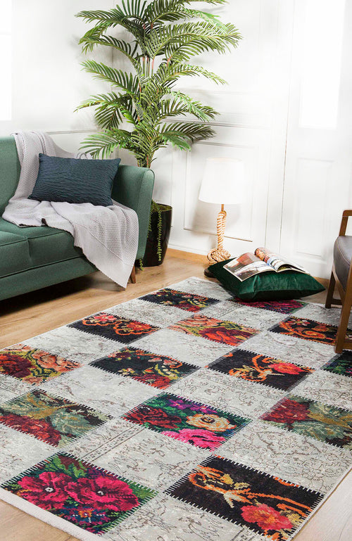 Load image 1 in gallery view. A cozy living room with a green sofa, gray blanket, pillow, large potted plant, floor lamp, magazines, and the Blooming Paradise - Washable Rug - JR188—a multicolor floral rug ideal for high-traffic areas on light wooden floors.