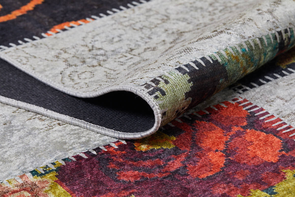 A close-up of the Blooming Paradise - Washable Rug - JR188 shows its folded edge, vibrant floral and geometric patterns in red, orange, green, and gray, and contrasting stitched borders—perfect for high-traffic areas.