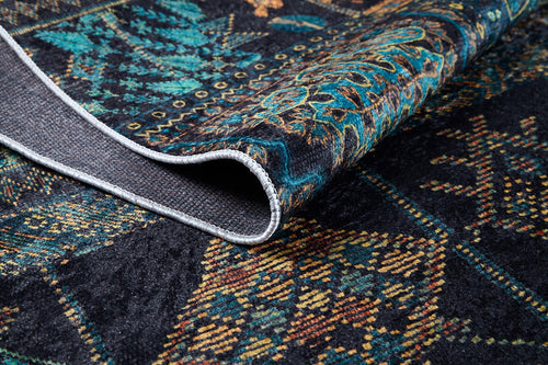 Load image 1 in gallery view. A close-up of the Blossoming Bazaar - Washable Rug (JR1862) in dark blue, featuring teal, gold, and orange patterns. One corner is folded to show its textured woven underside—durable for high-traffic areas and easy to wash.