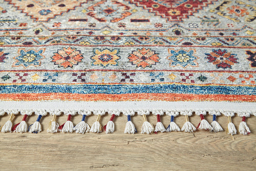 Load image 1 in gallery view. Close-up of the Bohemian Bouquet - Washable Rug - JR5090 shows its intricate geometric and floral edge, cream tassels, blue and red accents on a wooden floor. This washable rug adds vibrant style and easy care to any room.