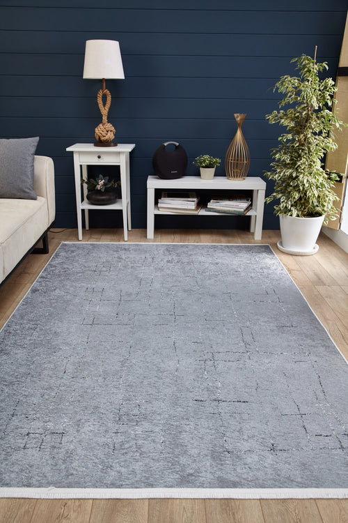 Bild 1 in Galerieansicht laden. A modern living room featuring the Bohemian Driftwood - Washable Rug - JR1951 in gray-anthracite on wood floors, paired with a white sofa, two white tables with decor, a lamp, books, and a potted plant against dark blue paneled walls.