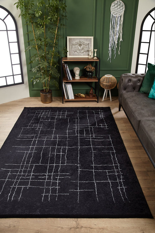 Load image 1 in gallery view. A modern living room features the Bohemian Illusion - Washable Rug - JR1953 in black with white lines, a gray tufted sofa with green pillows, a wooden bookshelf, a tall plant, and green paneled walls with decorative accents.