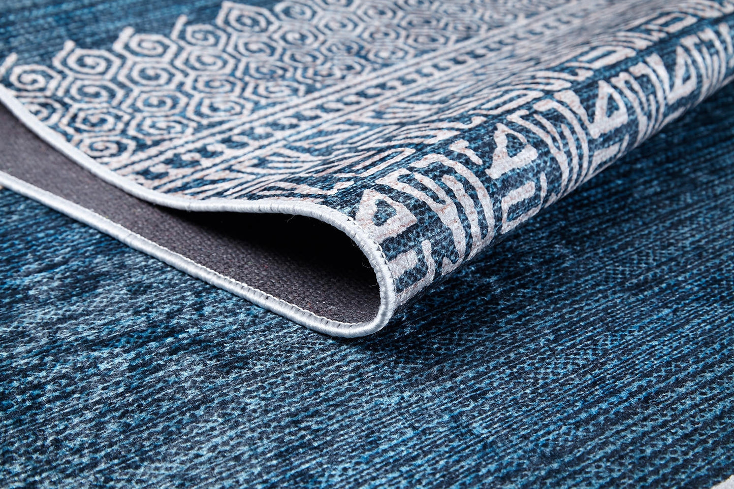A close-up of the Bohemian Retreat - Washable Rug - JR1589 shows blue tones with white geometric and abstract patterns, a folded corner revealing its texture—ideal as a washable rug for high-traffic areas.