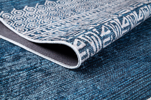 Load image 1 in gallery view. A close-up of the Bohemian Retreat - Washable Rug - JR1589 shows blue tones with white geometric and abstract patterns, a folded corner revealing its texture—ideal as a washable rug for high-traffic areas.