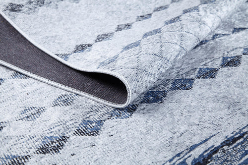 Bild 1 in Galerieansicht laden. A close-up of the Bohemian Reverie - Washable Rug - JR1974 (Outlet) US shows its light gray and blue pattern, a folded corner revealing the dark, textured backing and detailed weave—ideal for high-traffic areas.