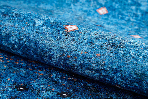 Load image 1 in gallery view. A close-up of the Bohemian Whirlwind - Washable Rug (JR1989) in blue, featuring red, white, and black square patterns on its textured, washable surface—ideal for high-traffic areas. The fabric is slightly folded in the foreground.