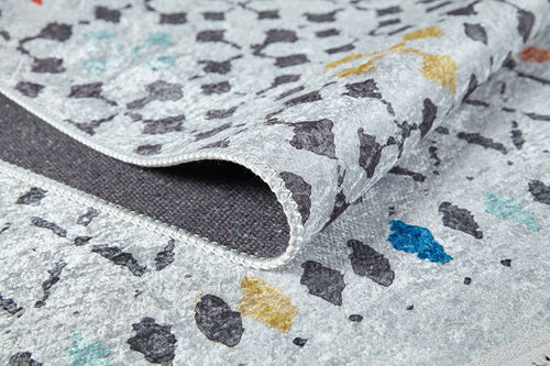 Load image 1 in gallery view. Close-up of the Boho Breeze - Machine-Washable Rug (JR5011), a flat weave with a light gray background and abstract black, yellow, blue, and turquoise shapes. The partially folded rug shows edge stitching and a dark underside.