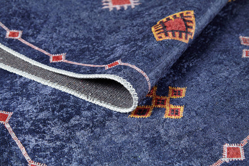 Load image 1 in gallery view. A close-up of the Boho Chic Tapestry - Washable Rug (JR5083), featuring blue, red, and yellow geometric patterns. The allergy-friendly rug is slightly folded to reveal its stitched edge and underside.