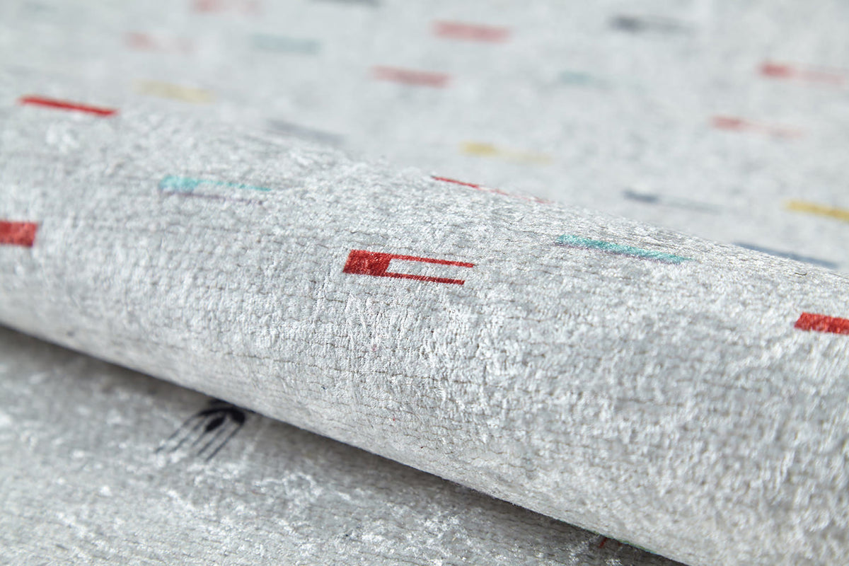 A close-up of the Boho Chic - Washable Rug - JR5103 reveals its textured, light gray surface with scattered red, teal, yellow, and black patterns. Slightly rolled to show detail—perfect for high-traffic areas.