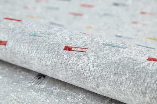 Load image 1 in gallery view. A close-up of the Boho Chic - Washable Rug - JR5103 reveals its textured, light gray surface with scattered red, teal, yellow, and black patterns. Slightly rolled to show detail—perfect for high-traffic areas.