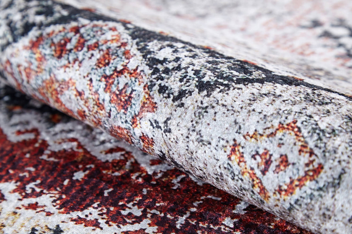 A close-up of the Boho Oasis - Washable Rug - JR1618 shows red, gray, black, and yellow geometric designs. Partially rolled, this gray-anthracite rug is washable and ideal for high-traffic areas with its detailed texture and motifs.