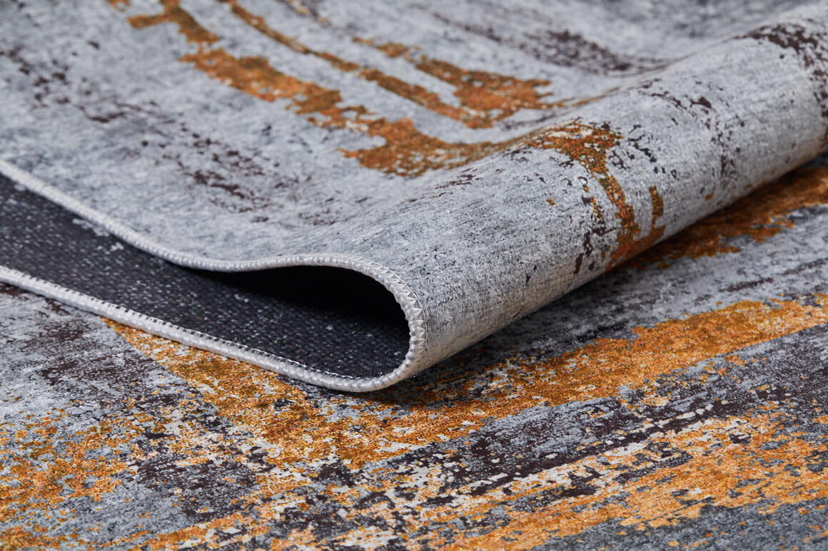 A close-up of the Bold and Chic - Washable Rug - JR1198, featuring modern abstract gray, orange, and brown patterns with a lifted edge to show texture—perfect for allergy-sensitive spaces.