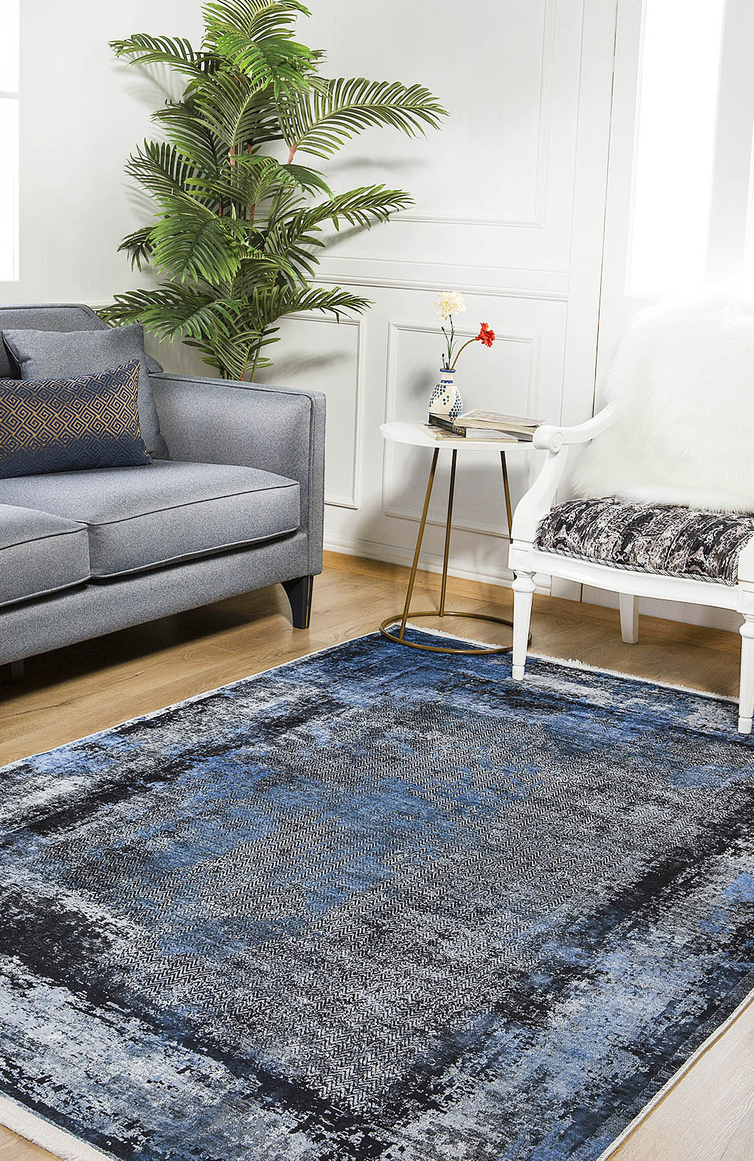 A modern living room features a gray sofa, white chair with a throw, and the Bold and Minimalist - Washable Rug - JR1229, perfect for high-traffic areas. A small side table with flowers and a green potted plant freshen up the white walls.