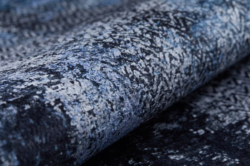 Load image 1 in gallery view. Close-up of the Bold and Minimalist - Washable Rug - JR1229, featuring a rolled-up textured surface with an abstract marbled pattern in blue, gray, and black—ideal for high-traffic areas seeking a stylish, weathered look.
