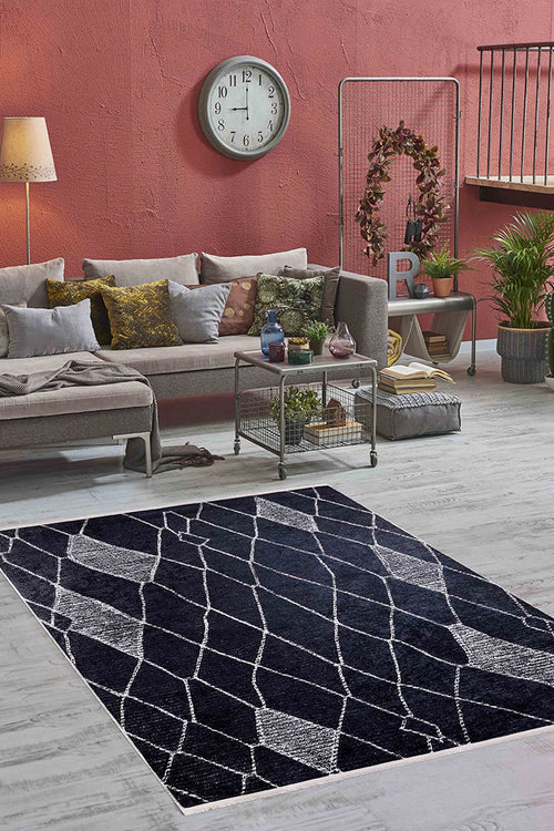 Load image 1 in gallery view. A modern living room with a gray sectional, assorted pillows, floor lamp, wall clock, potted plants, and the Byzantine Beauty - Washable Rug - JR1037 in black—ideal for high-traffic areas on light wood floors. The wall is muted red.