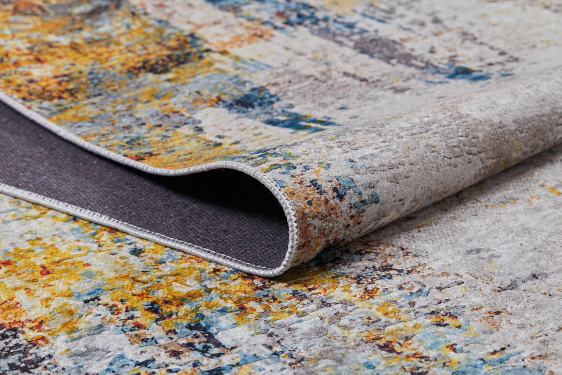 A close-up of the Chromatic Kaleidoscope - Washable Rug - JR1483 displays its multicolored abstract patterns in yellow, blue, orange, and gray with a folded corner revealing the dark underside—ideal for high-traffic spaces.
