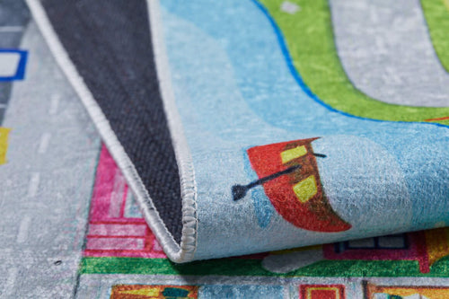 Bild 1 in Galerieansicht laden. A close-up of the City Adventure - Machine-Washable Rug JRC039, featuring roads, grass, buildings, and a boat design; shown partially folded to display its black textured underside.