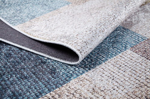 Load image 1 in gallery view. Close-up of the Classic Check - Washable Rug - JR1955 with a folded corner, displaying its blue, gray, and beige patchwork. Perfect for allergy-sensitive homes and high-traffic areas, featuring detailed texture and visible stitching.