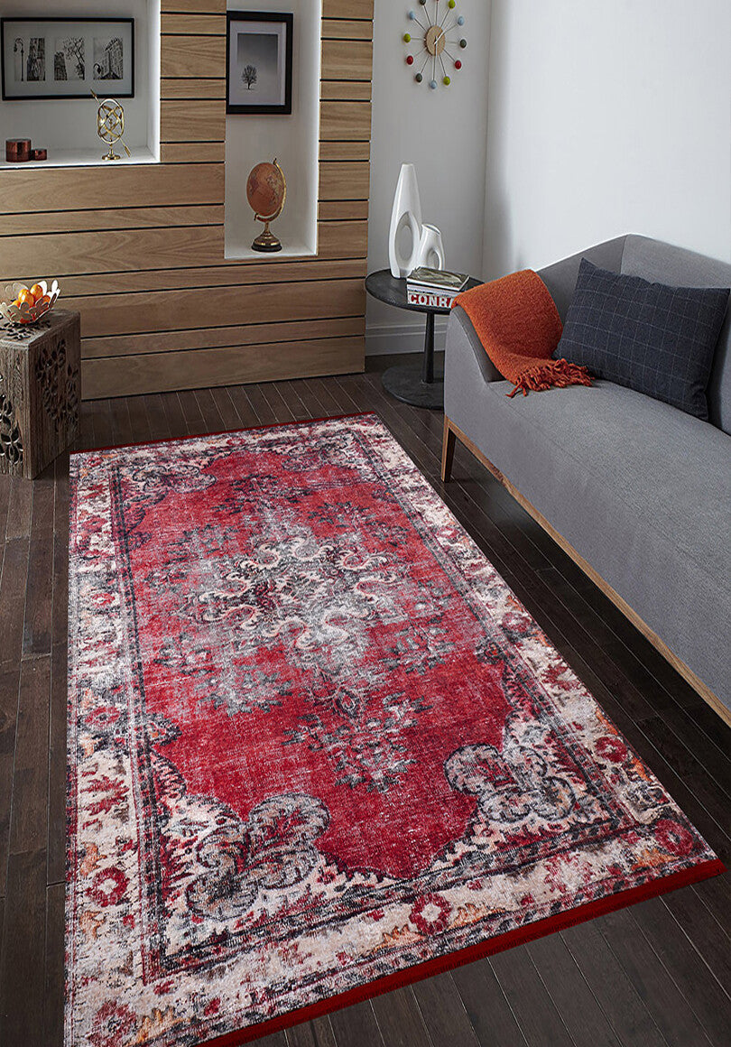 A modern living room with dark wood floors, a gray sofa with an orange throw, and the Classic Revival - Washable Rug - JR1374—ideal for high-traffic areas. Built-in wall shelves display decorative items and books.