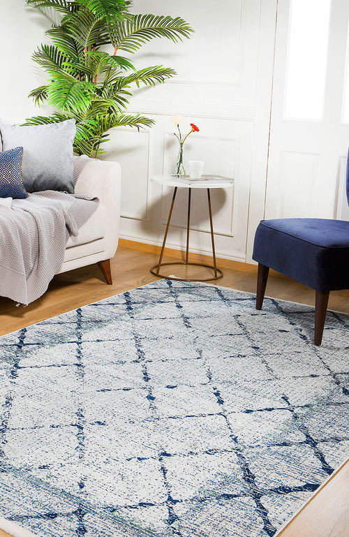 Load image 1 in gallery view. A cozy living room with a white sofa, blue cushioned chair, leafy plant, small round side table with flowers, and the Classic Trellis - Washable Rug - JR710 on a wooden floor, illuminated by sunlight streaming through a window.