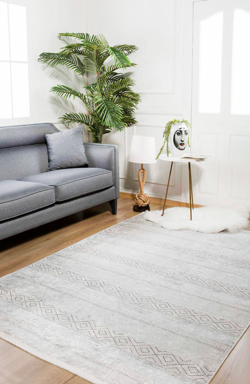 Load image 1 in gallery view. A modern living room with a gray sofa, cushion, tall green plant, face vase with trailing leaves on a table, decorative lamp, and the large Contemporary Coordinates - Washable Rug - JR750 in cream and beige on the wooden floor.