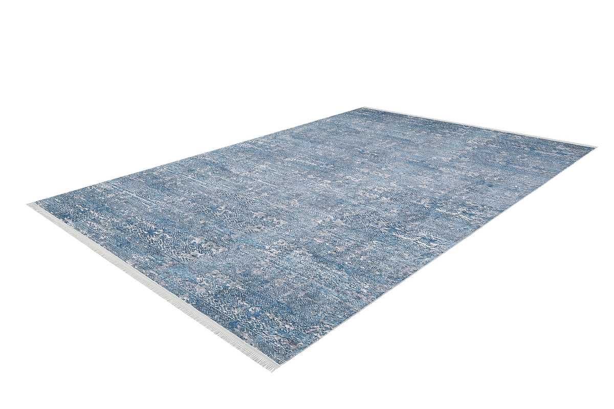 The Contemporary Serenity - Machine-Washable Rug JR1884 is a large rectangular blue rug featuring a subtle distressed pattern, short white fringe on the short edges, and is ideal for high-traffic areas. Shown angled against a white background.