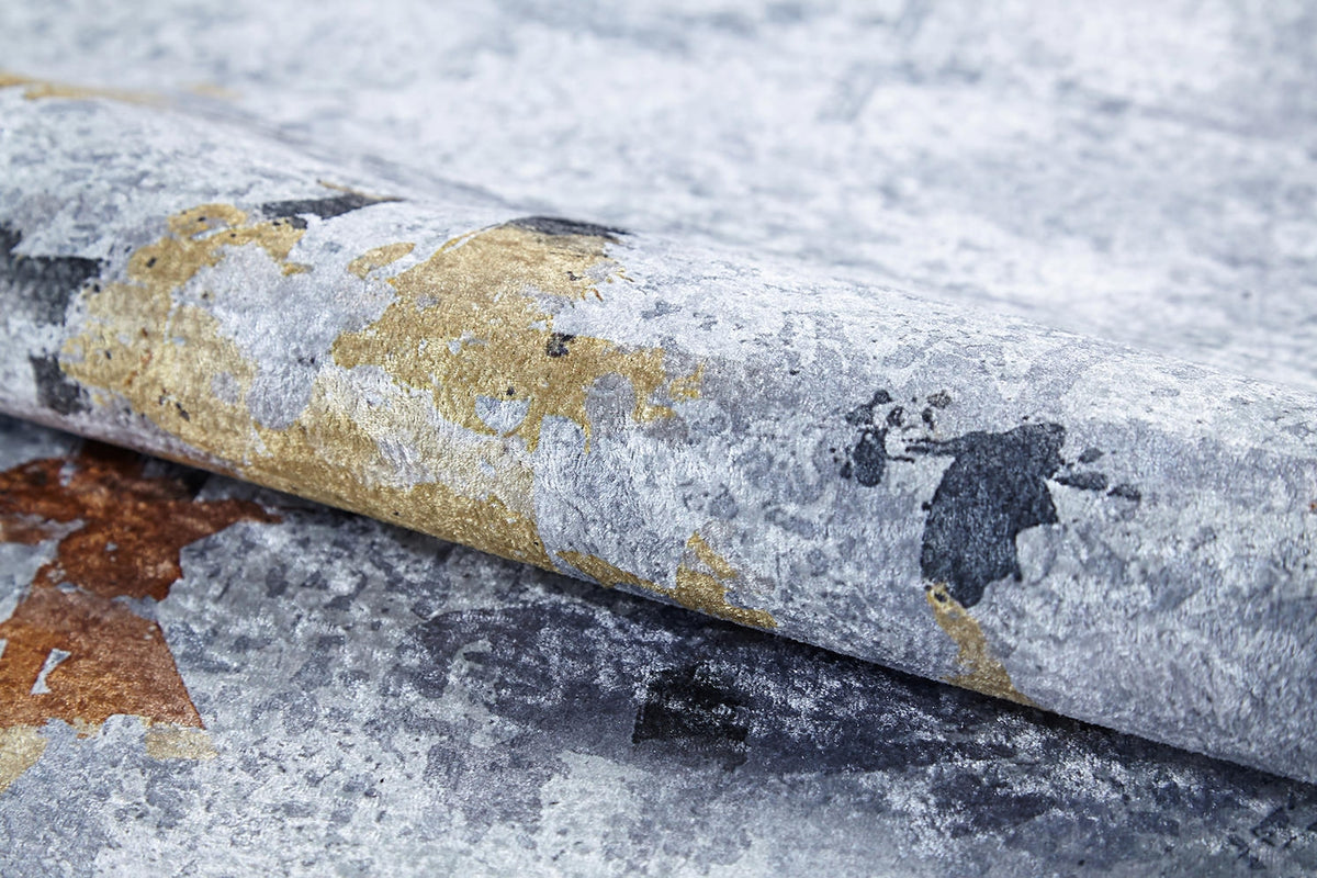 A close-up of the Cross Country - Washable Rug (JR1753) featuring an abstract, weathered pattern in gray, gold, brown, and black—ideal for high-traffic areas and reminiscent of peeling paint or a distressed finish.