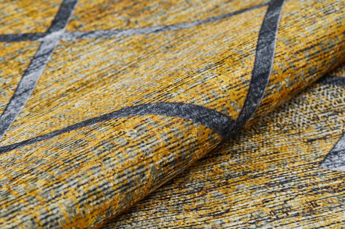 A close-up of the Crossed Connections - Washable Rug - JR1181 shows its yellow and gray geometric design with intersecting dark gray lines. Slight fabric folds highlight its texture. Ideal for high-traffic areas and easy to clean.