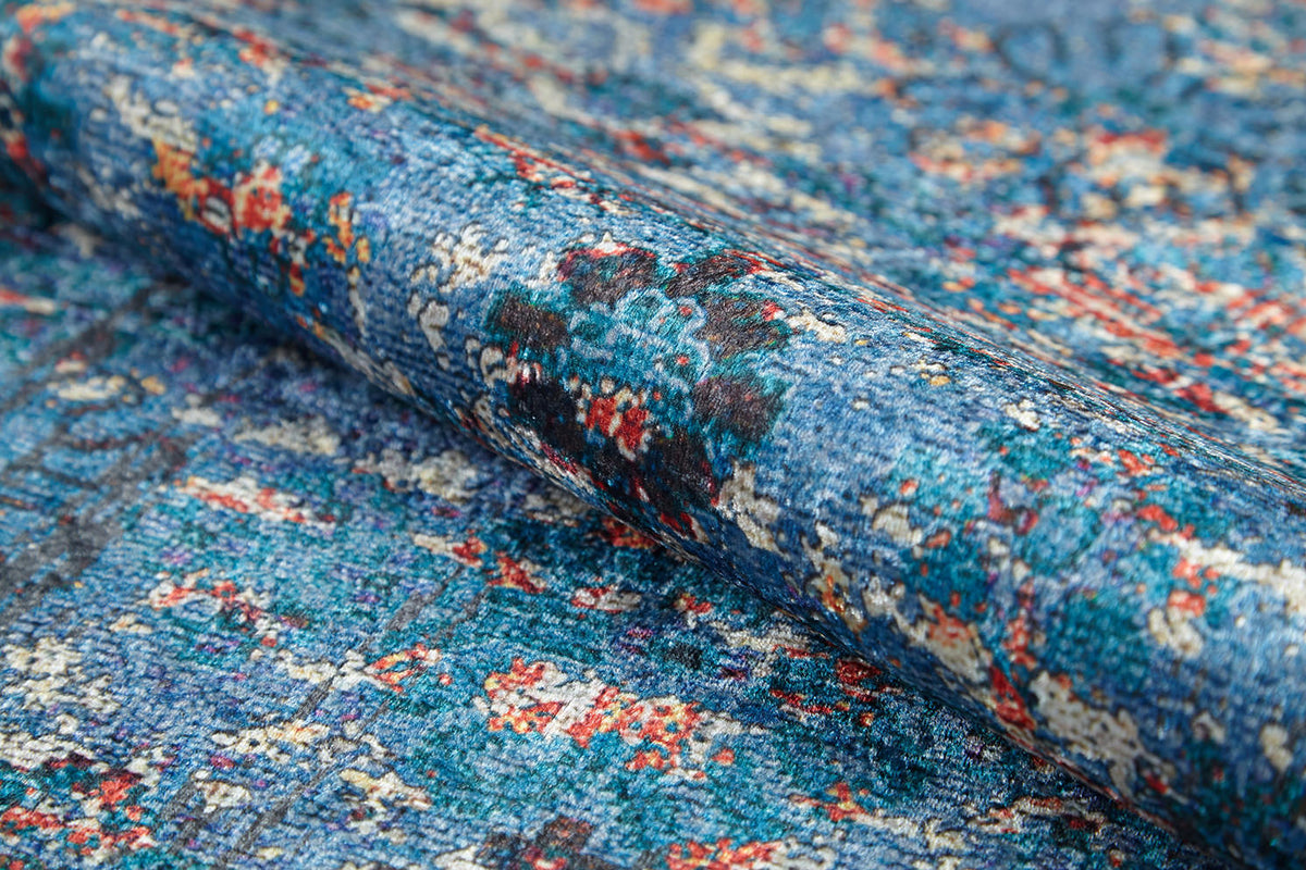 A close-up of the Desert Diamond - Washable Rug - JR5071, rolled to display its textured fabric and abstract floral design in blue, red, white, and black—ideal for high-traffic areas.