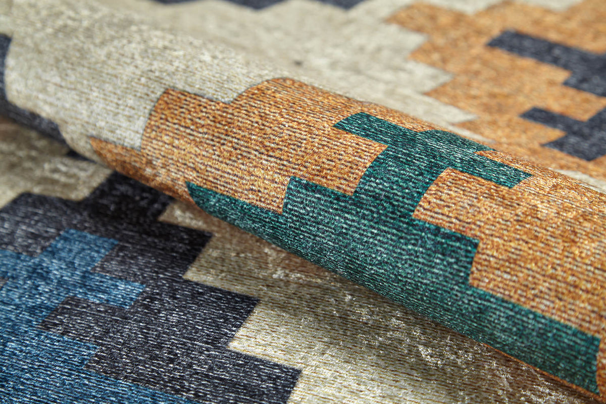 A close-up of the Desert Mirage - Washable Rug - JR5033 highlights its green, gold, navy blue, and beige geometric pattern and flat weave texture.