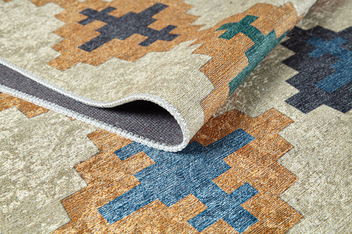 Load image 1 in gallery view. A close-up of the Desert Mirage - Washable Rug (JR5033), a flat weave with geometric shapes in blue, green, brown, and black on beige. The washable rug is slightly folded to display its edge and thickness.