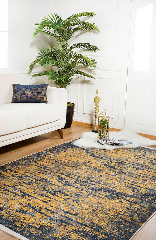 Load image 1 in gallery view. A modern living room featuring a white sofa, the Diagonal Dash - Washable Rug - JR1310 in blue and gold for high-traffic areas, a green potted plant, a decorative gold sculpture, magazines, and a fluffy white rug on wooden floors.