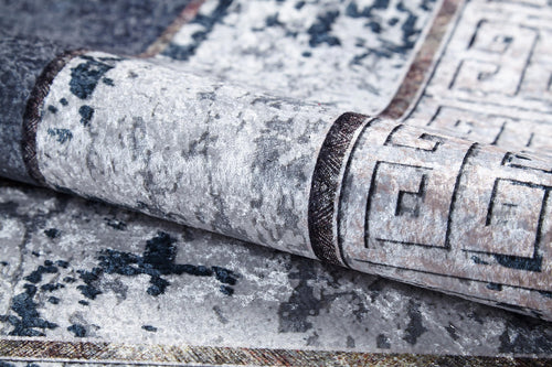 Load image 1 in gallery view. A close-up of the Dramatic Boundaries - Washable Rug (JR1810), folded to show its gray, textured, mottled pattern and geometric border in dark and light tones—perfect for high-traffic areas.