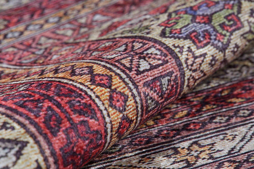 Load image 1 in gallery view. A close-up of the Elegant Embellishments - Washable Rug - JR43 displays geometric patterns in red, yellow, green, black, and beige. Slightly folded to reveal its texture, this rug is ideal for high-traffic areas and easy to clean.