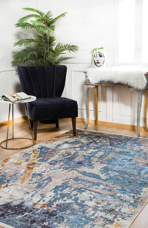 Load image 1 in gallery view. A modern room featuring the Enigmatic Elegance - Washable Rug - JR787, a blue velvet chair, round table with open magazine, plant, white fur-covered desk, and decorative vase brings style and function to high-traffic areas.