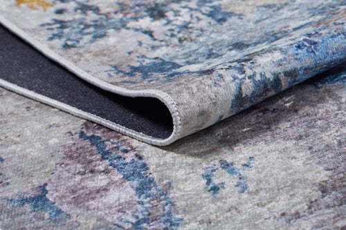 Load image 1 in gallery view. A close-up of the Enigmatic Elegance - Washable Rug - JR787, folded to reveal its textured abstract pattern in blue, gray, and purple tones with visible edge and underside—perfect for high-traffic areas.