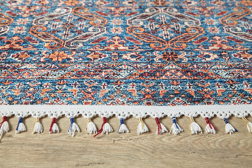 Load image 1 in gallery view. A close-up of the Ethereal Essence - Washable Rug - JR5087, a colorful flat weave with intricate blue, red, and orange geometric and floral designs, plus white fringe tassels with red and blue accents, shown on a wooden floor.