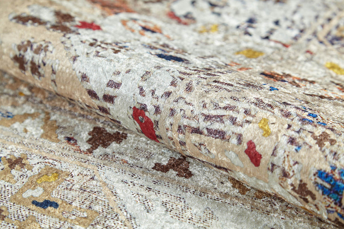 A close-up of the Ethno Expanse - Machine-Washable Rug (JR5046) shows its textured, abstract woven pattern in beige, brown, red, blue, and yellow. Slightly folded to display thickness—ideal for high-traffic areas and simple to clean.